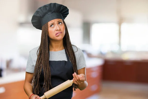 Portrait of a young black baker woman doubting and confused, thinking of an idea or worried about something