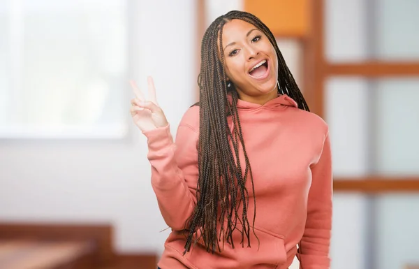 Portrait of a young black woman wearing braids fun and happy, positive and natural, makes a gesture of victory, peace concept