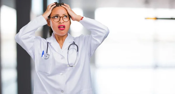 Portrait of a young black doctor woman worried and overwhelmed, forgetful, realize something, expression of shock at having made a mistake