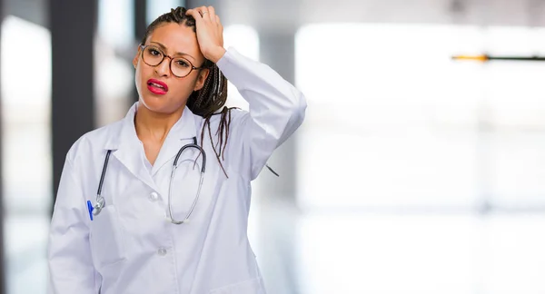 Portrait of a young black doctor woman worried and overwhelmed, forgetful, realize something, expression of shock at having made a mistake