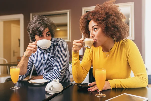 Young couple drinking coffee and an orange juice, looking at each other. They are happy and comfortable.