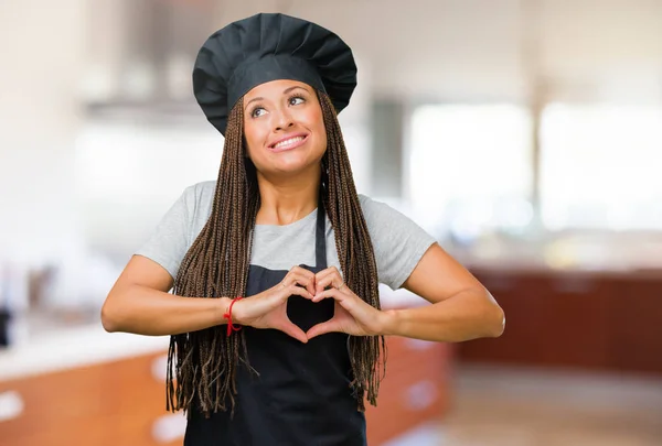 Portrait of a young black baker woman making a heart with hands, expressing the concept of love and friendship, happy and smiling