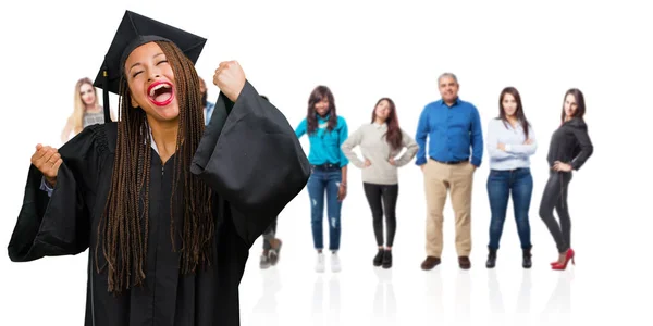 Young graduated black woman wearing braids very happy and excited, raising arms, celebrating a victory or success, winning the lottery