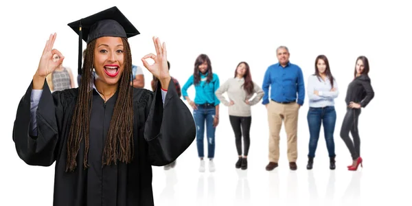 Young graduated black woman wearing braids cheerful and confident doing ok gesture, excited and screaming, concept of approval and success