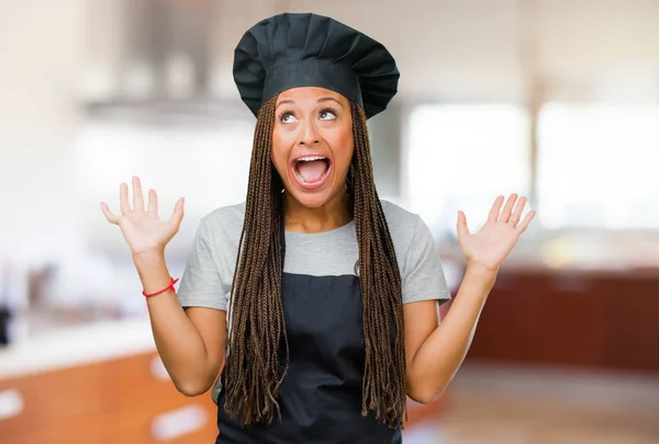 Portrait of a young black baker woman screaming happy, surprised by an offer or a promotion, gaping, jumping and proud