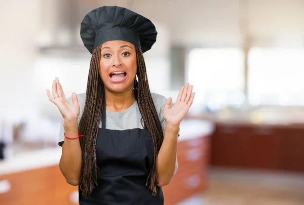 Portrait of a young black baker woman surprised and shocked, looking with wide eyes, excited by an offer or by a new job, win concept