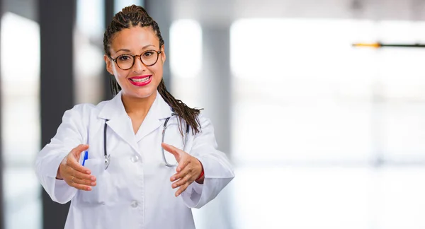 Portrait of a young black doctor woman reaching out to greet someone or gesturing to help, happy and excited