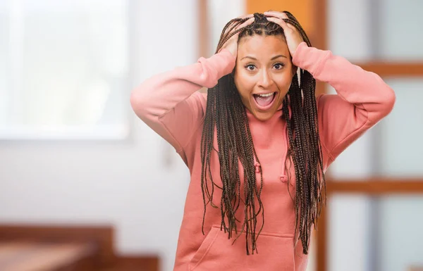 Portrait of a young black woman wearing braids frustrated and desperate, angry and sad with hands on head
