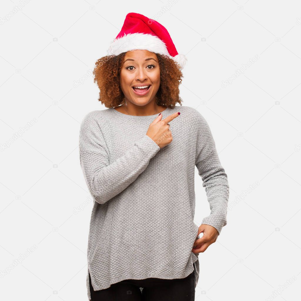 Young black woman wearing a santa hat smiling and pointing to the side