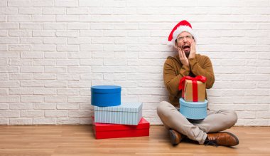 Young man sitting with gifts celebrating christmas desperate and sad clipart