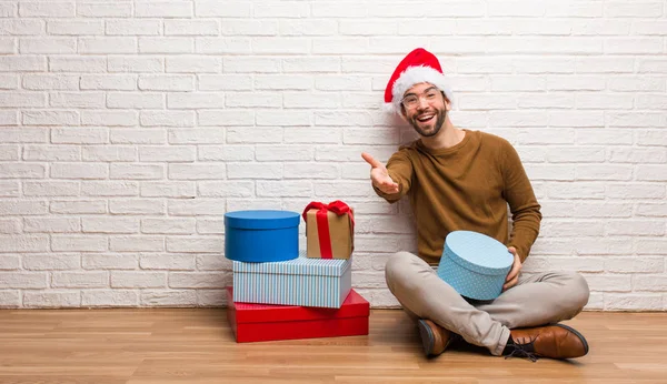 Young man sitting with gifts celebrating christmas reaching out to greet someone