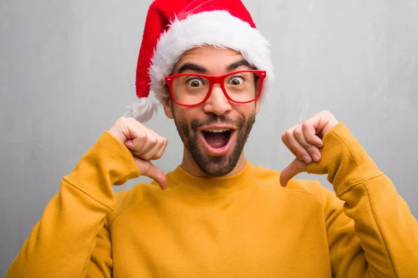 若い男は祝うクリスマスの日指を指して 贈り物を保持している例に従う — ストック写真