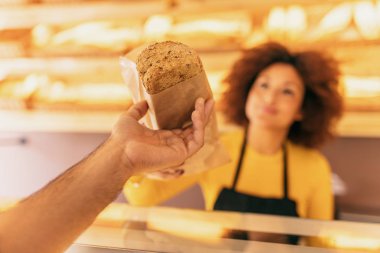 Bir istemci, gülümseyen ve mutlu bir tahıl ekmek sopa veren genç afro kadın baker bir fırın içinde.