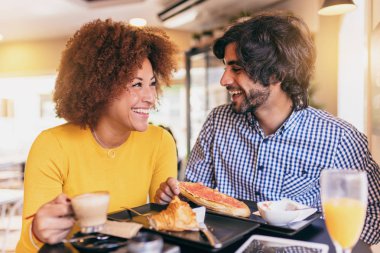 Genç çift kafede kahvaltı iyi. Onlar portakal suyu içme ve yeme bir kruvasan ve tost ekmeği. Gülen ve having fun.