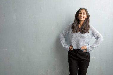 Eller genç Hintli kadın ile bir grunge duvara ayakta, rahat ve gülümseyen, çok olumlu ve neşeli kalçalarına