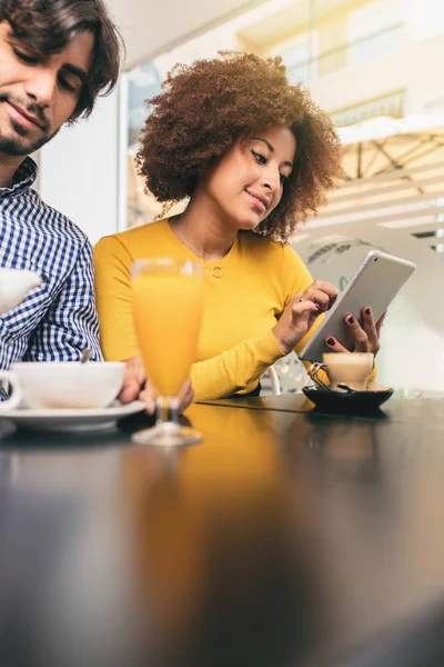 咖啡馆里的一对夫妇很放松 喝着茶 咖啡和橙汁 非洲女人正在用平板电脑 面带微笑 — 图库照片
