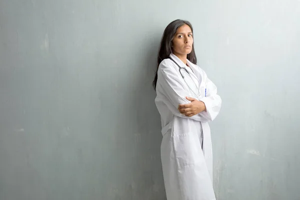 Young indian doctor woman against a wall crossing his arms, serious and imposing, feeling confident and showing power