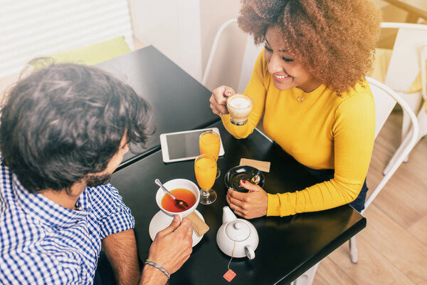 Young couple having a breakfast at a coffee shop, drinking tea and coffee. View from above.