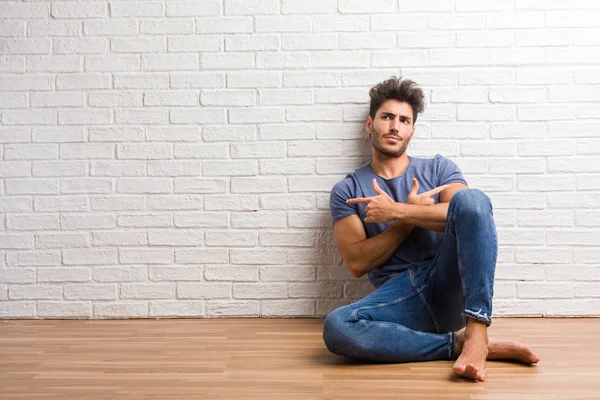 Young natural man sit on a wooden floor confused and doubtful, decide between two options, concept of indecision