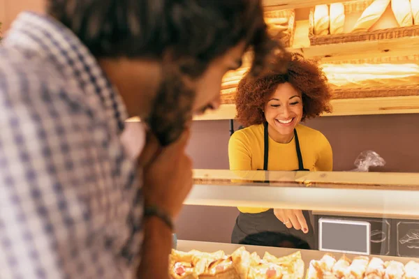 Young man buying something in a bakery, is being attended by an pretty afro woman.