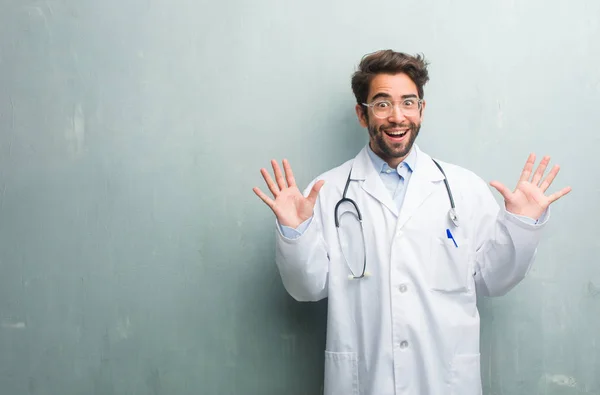 Young friendly doctor man against a grunge wall with a copy space screaming happy, surprised by an offer or a promotion, gaping, jumping and proud