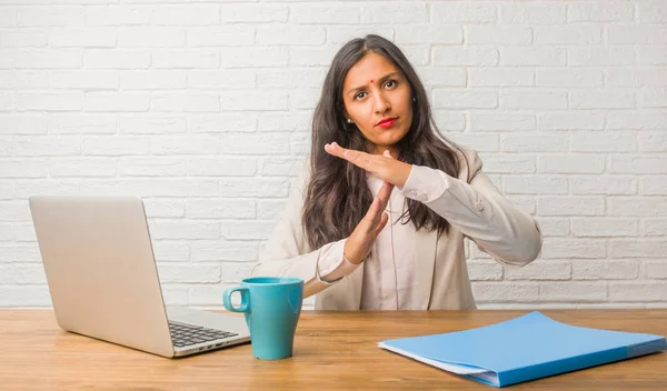 Young indian woman at the office tired and bored, making a timeout gesture, needs to stop because of work stress, time concept
