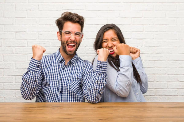 Young indian woman and caucasian man couple very happy and excited, raising arms, celebrating a victory or success, winning the lottery