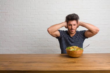 Eller, kızgın ve bazı ses işitme yorgun kulaklarıyla kapsayan bir masada oturan genç yakışıklı ve doğal adam. Taze bir salata yemek.