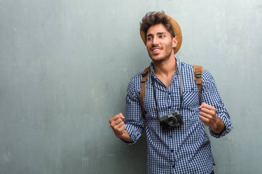 Silah, bir zafer ya da başarı, kutlama yükselterek bir hasır şapka, bir sırt çantası ve bir fotoğraf makinesi çok mutlu ve heyecanlı, genç yakışıklı gezgin adam Piyango kazanma