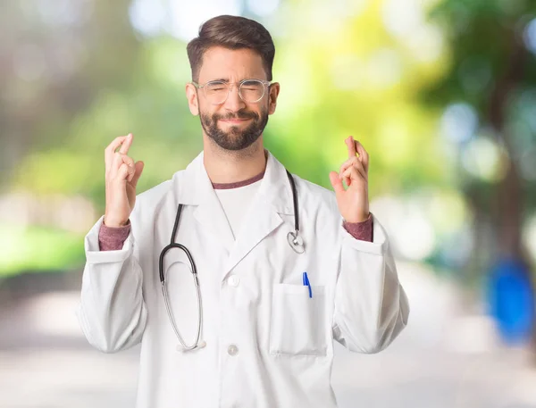 Young doctor man crossing fingers for having luck