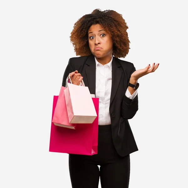 Young Black Woman Holding Shopping Bags Doubting Shrugging Shoulders — Stock Photo, Image