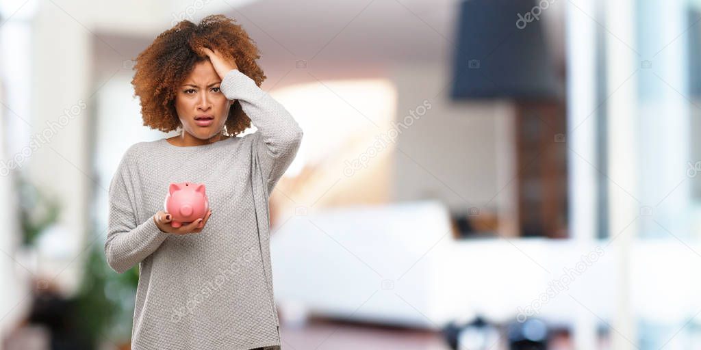 Young black woman holding piggy bank tired and very sleepy