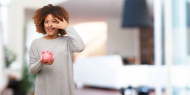 Utandım ve aynı anda gülüyor kumbara tutan genç siyah kadın