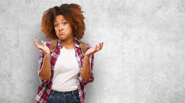 Young traveler black woman doubting and shrugging shoulders