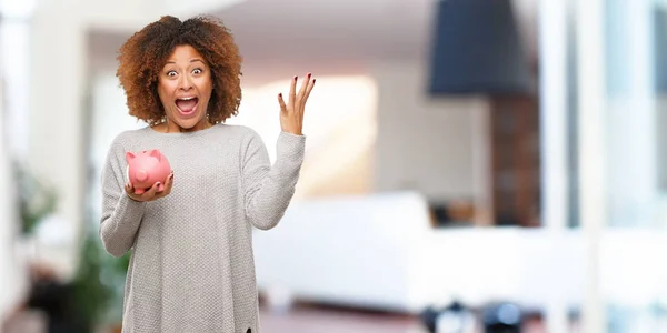 Young black woman holding piggy bank celebrating a victory or success