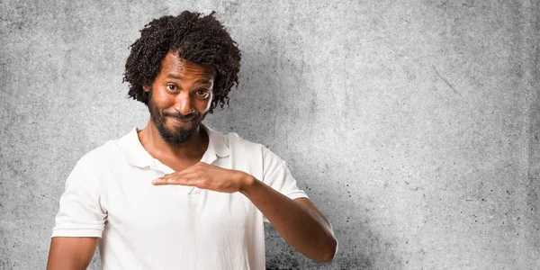 Handsome african american holding something with hands, showing a product, smiling and cheerful, offering an imaginary object