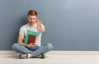 Genç redhead öğrenci önünde el koyarak katta oturan adam. Kitap tutuyor.