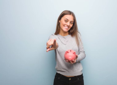 Genç oldukça beyaz kadın neşeli ve gülümseyerek açık için işaret. O bir kumbara tutuyor.