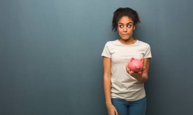 Genç siyah kadın hakkında bir fikir düşünüyorum. O bir kumbara tutuyor.