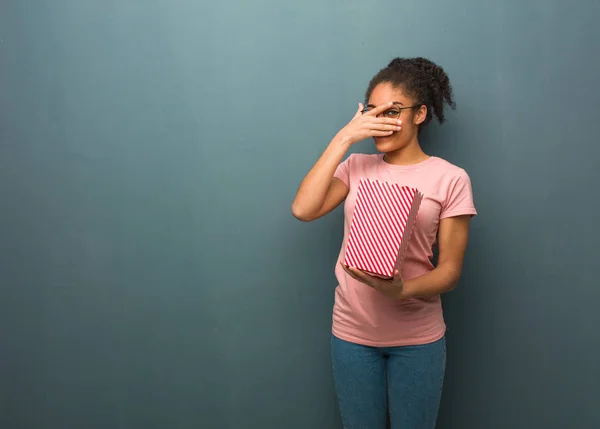 Young black woman embarrassed and laughing at the same time. She is holding a popcorns bucket.