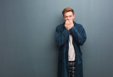 Genç redhead erkekte ağzını elleriyle kapsayan bir konuda gülüyor pijama