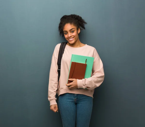 Young student black woman cheerful with a big smile. She is holding books.