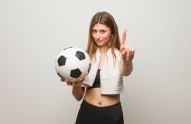 Bir numara gösteren genç Fitness Rus kadın. Bir futbol topu tutarak.