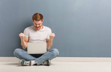 Yerde oturan genç Kızıl saçlı öğrenci adam sürpriz ve şok. O bir laptop tutuyor.