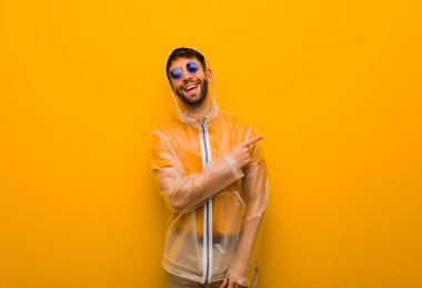 Genç adam parmak ile yan işaret eden bir yağmur ceket giyiyor