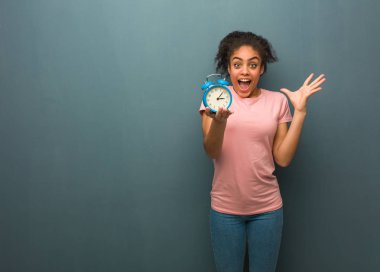 Young black woman celebrating a victory or success. She is holding an alarm clock.