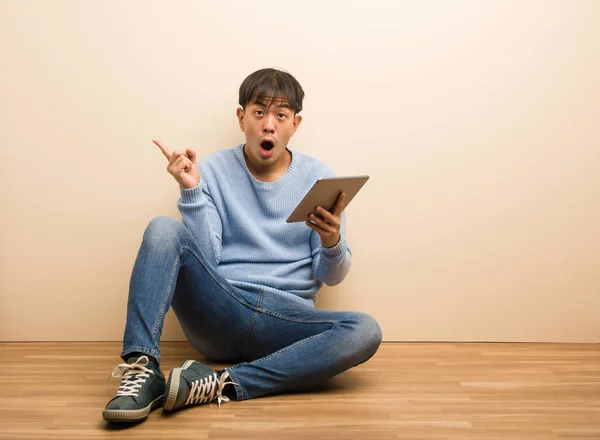 Jovem Chinês Sentado Usando Seu Tablet Apontando Para Lado — Fotografia de Stock