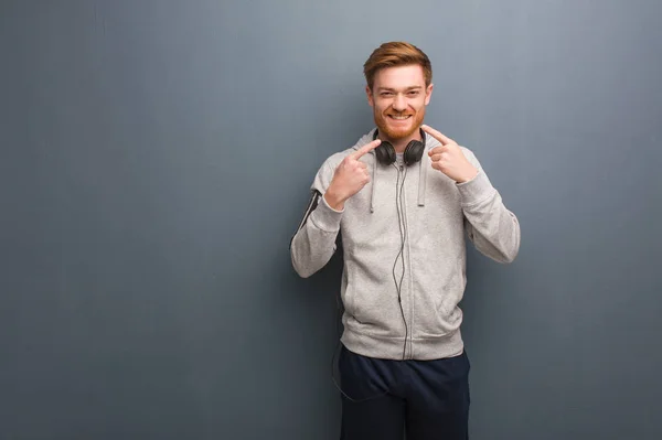 Young fitness redhead man smiles, pointing mouth