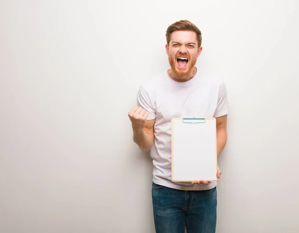 Young redhead man surprised and shocked. He is holding a clipboard.