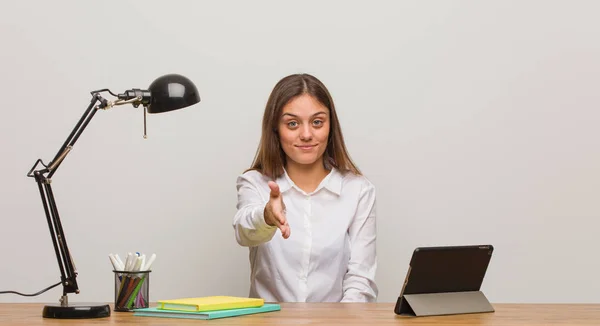 Young student woman working on her desk reaching out to greet someone